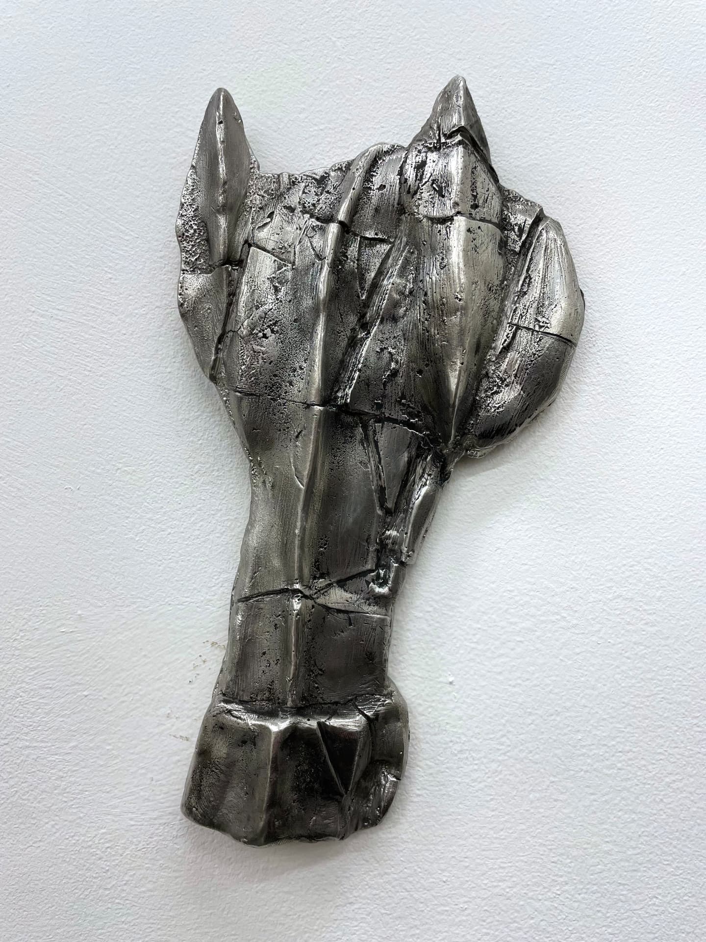Sand cast tin horse mask mounted on a white wall