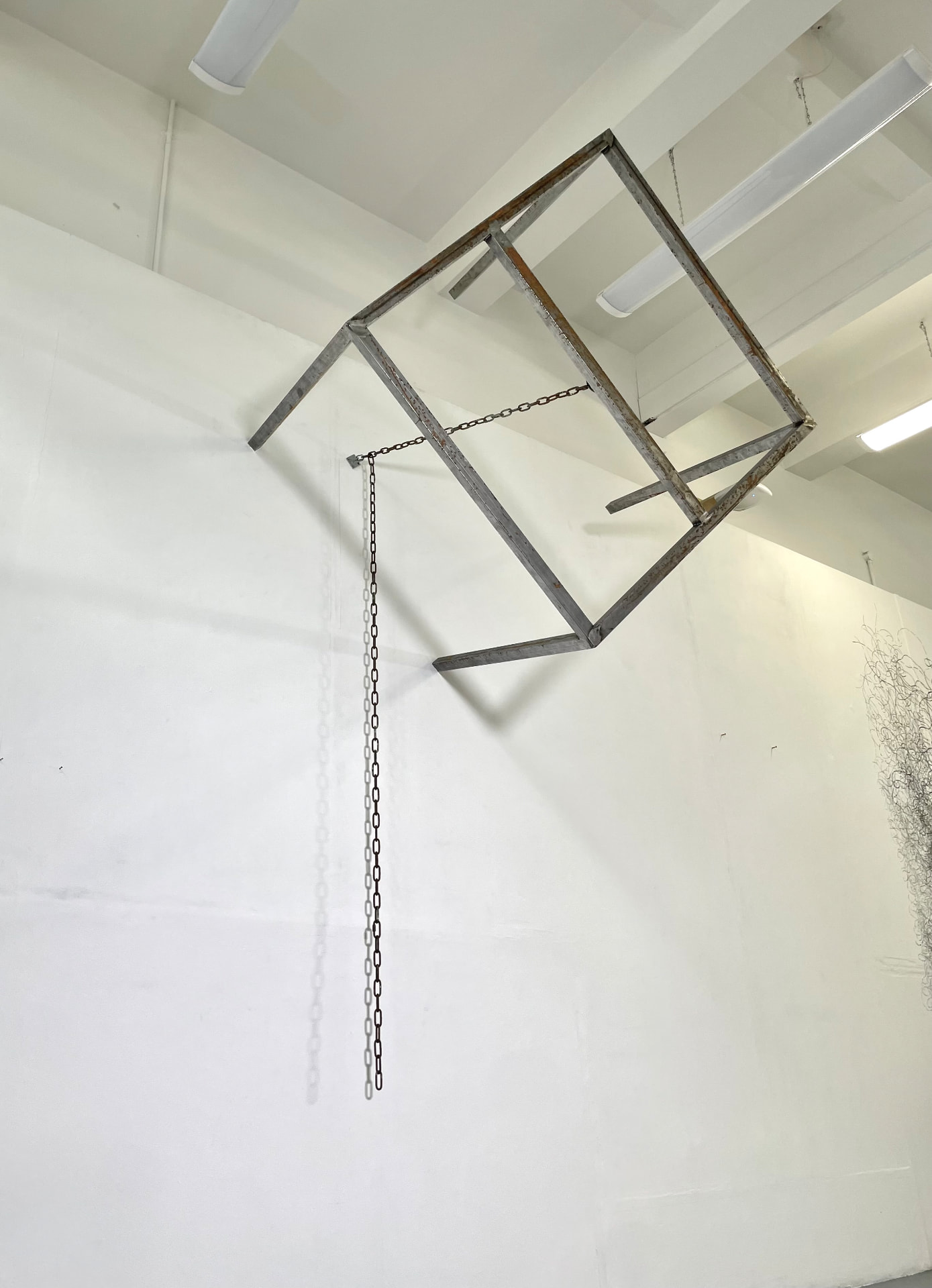 Suspended steel frame with chain hanging in a white gallery space
