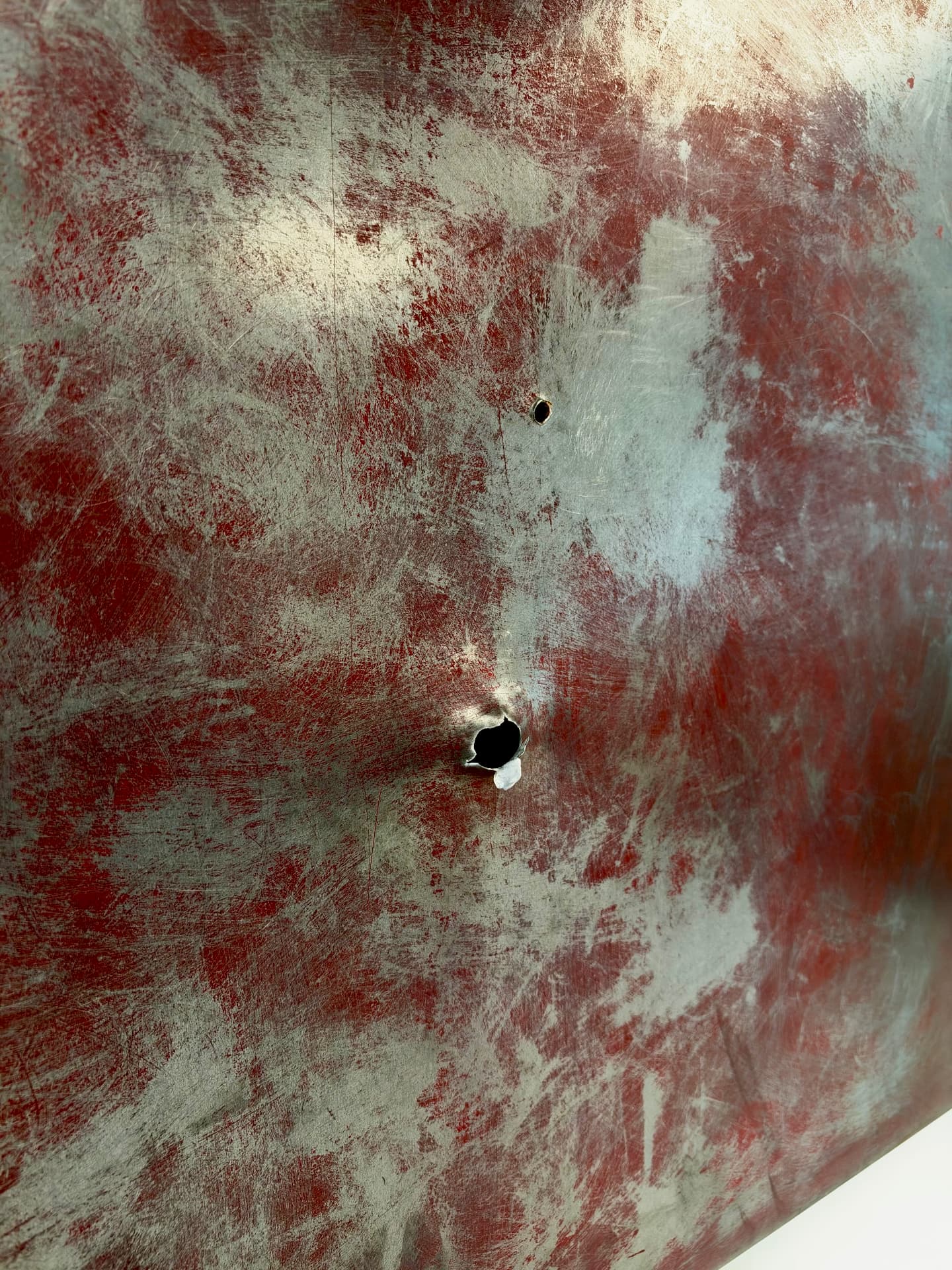 Close angled view of the scuffed red and silver surface with the two punctures