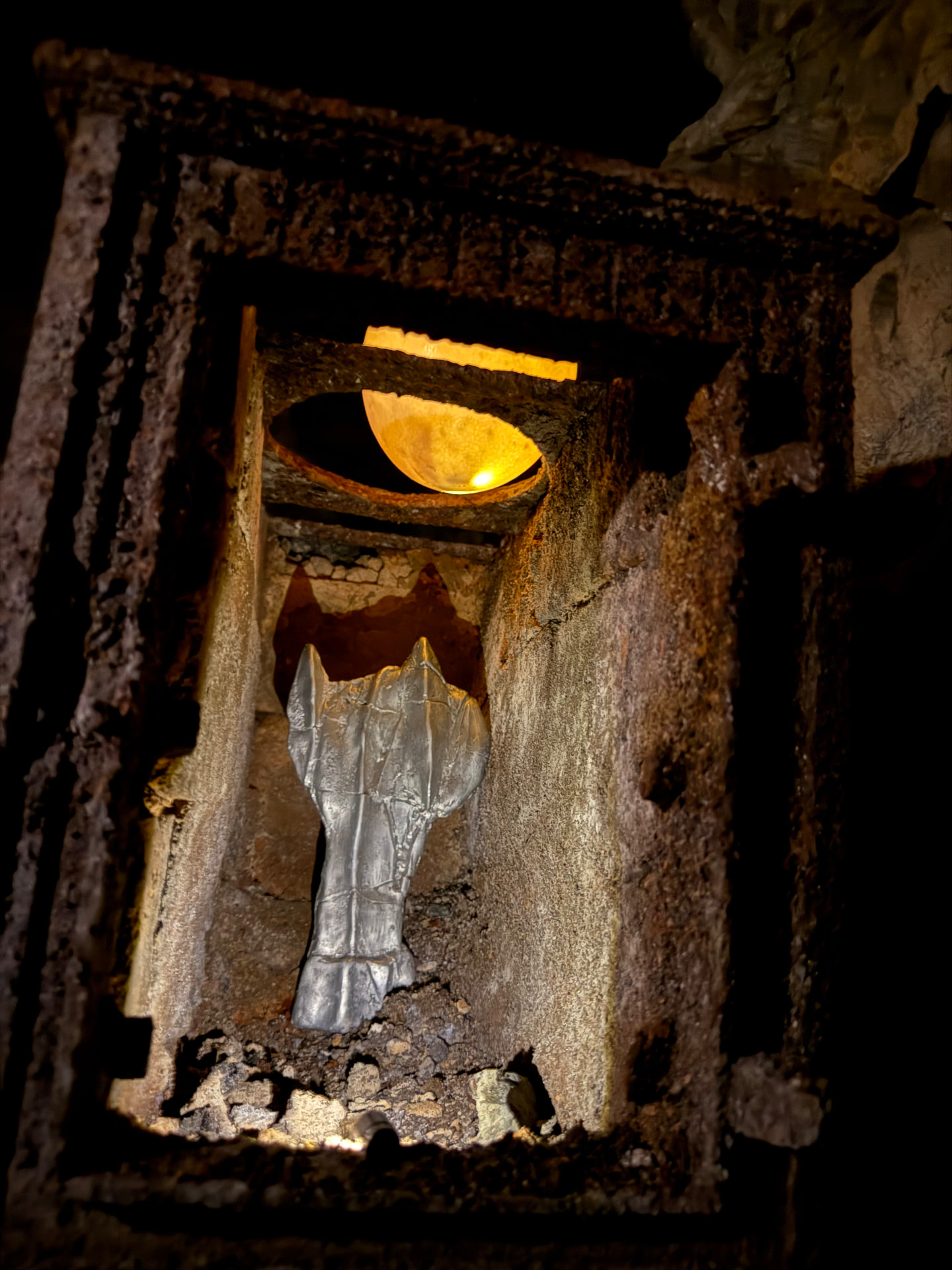 Tin sculpture standing inside a broken stone niche in the cave