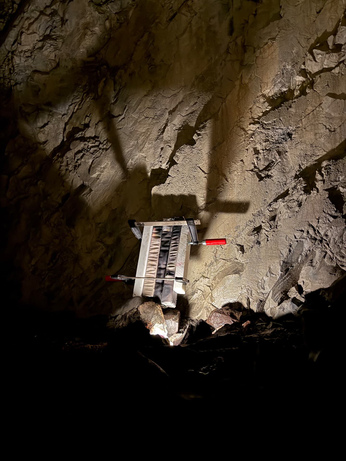 White clamped panel held against the cave wall by red-handled clamps