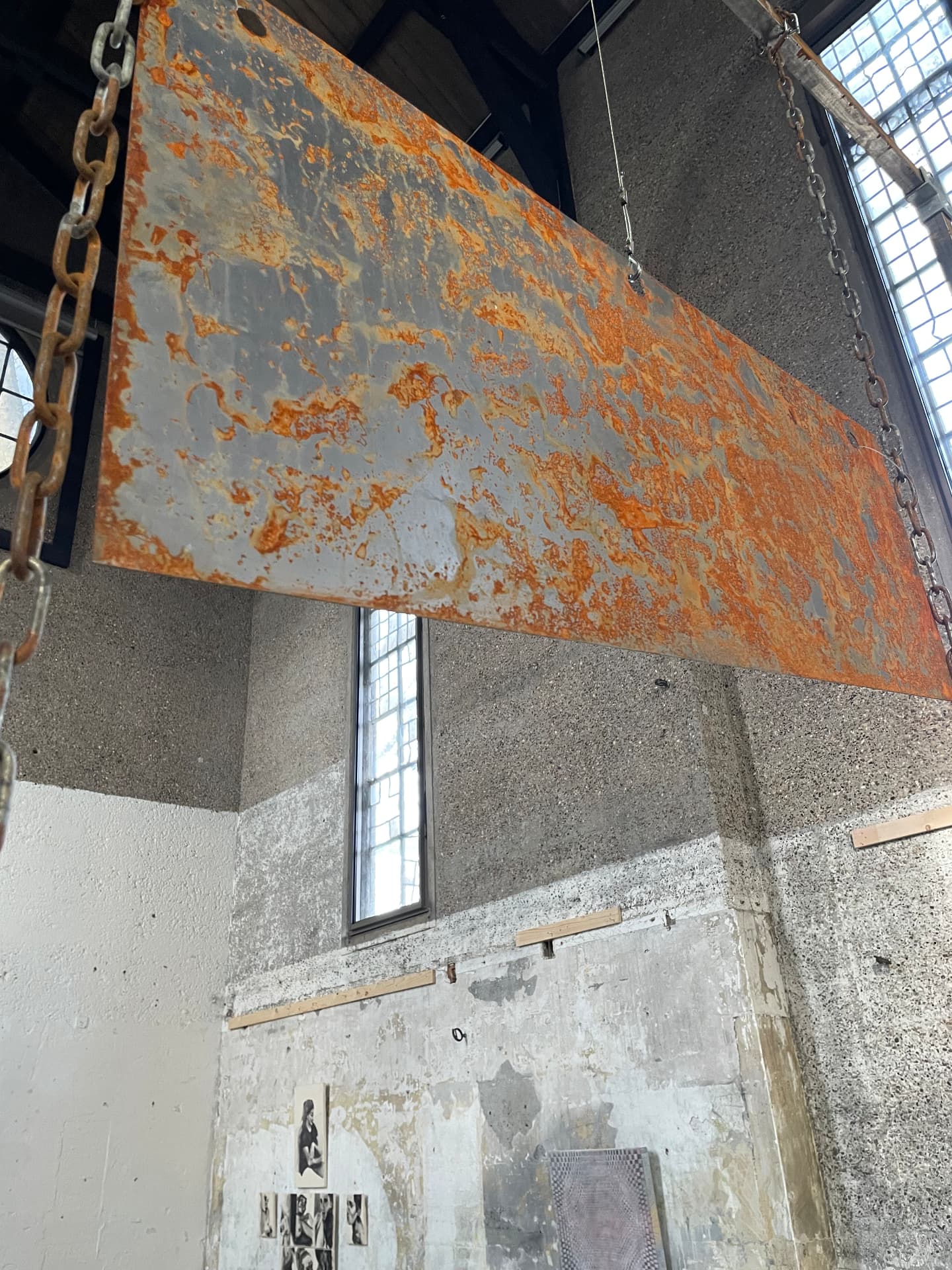Rusted steel panel suspended by chains in a tall concrete space