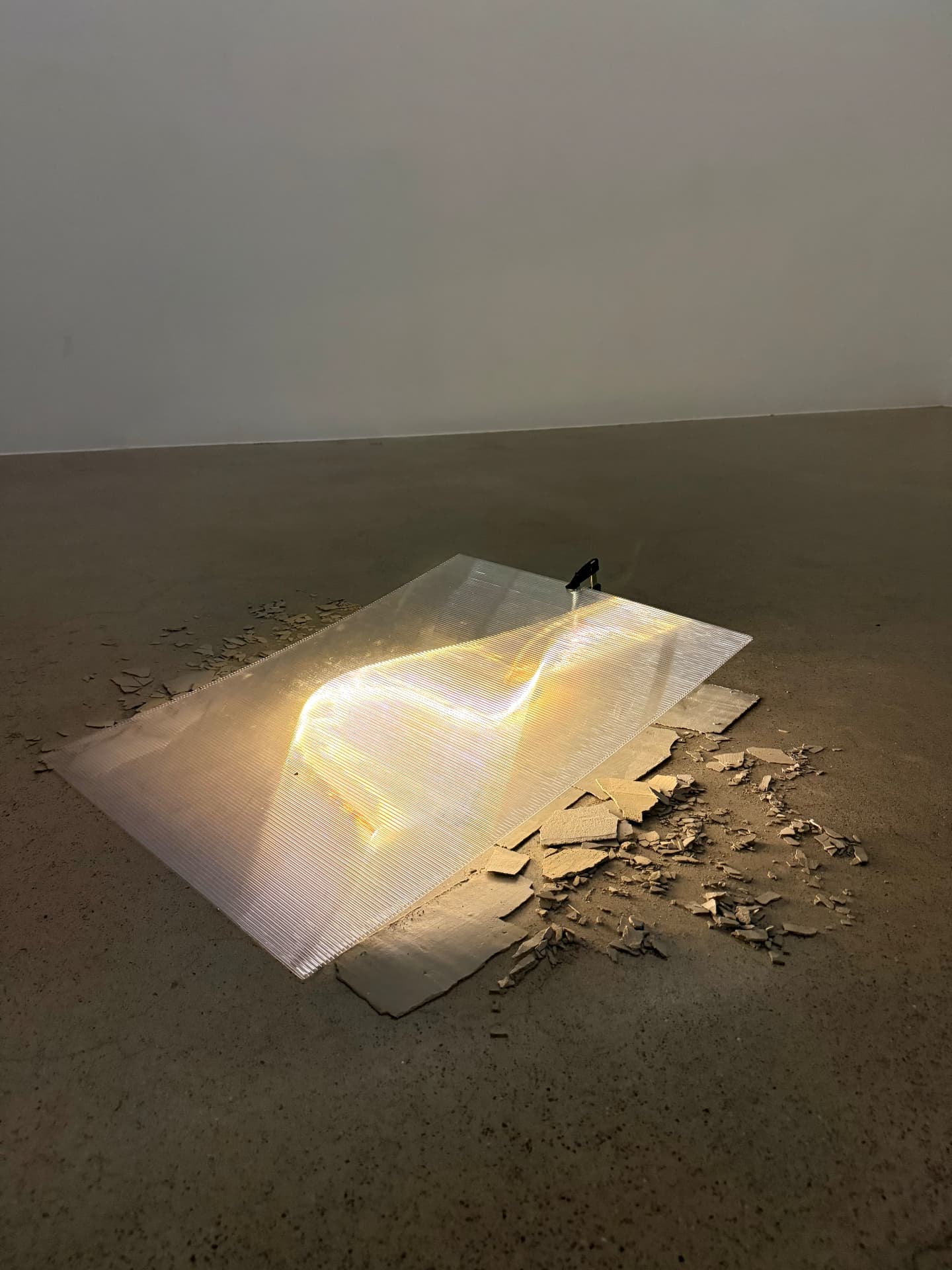 Lit polycarbonate sheet lying on a concrete floor among plaster fragments