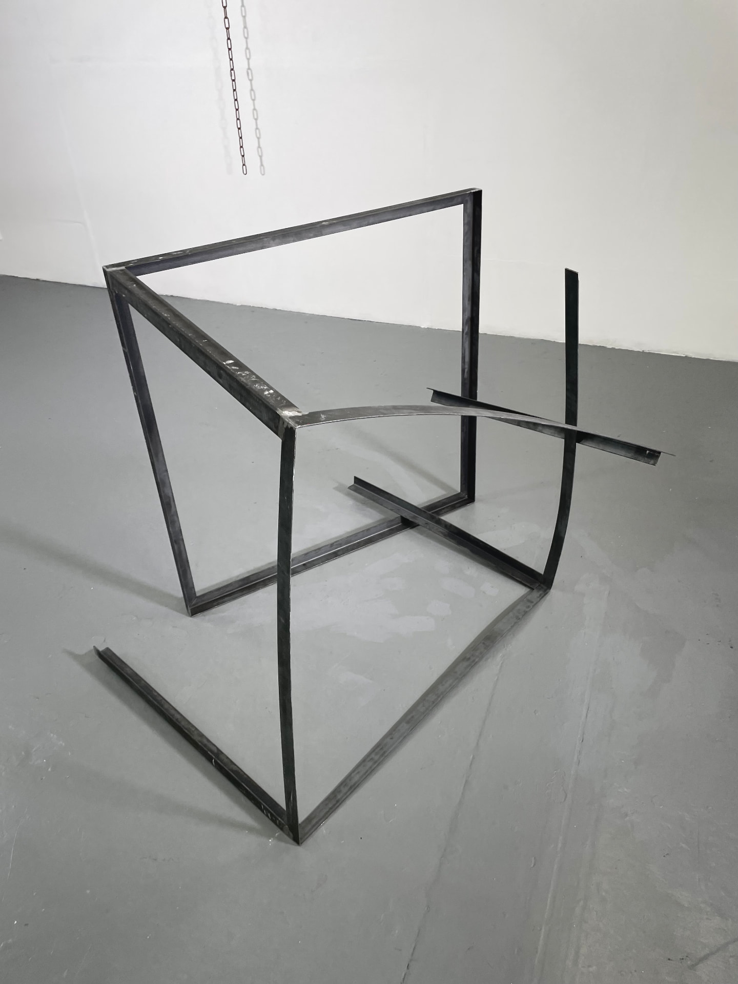Steel frame sculpture resting on a grey studio floor