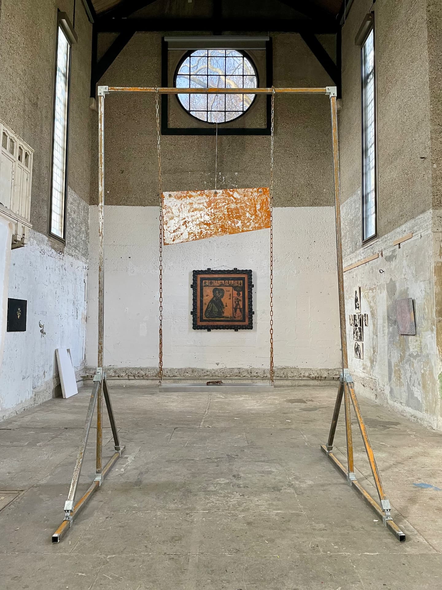 Steel gantry frame suspending a rusted metal panel by chains in a chapel-like space
