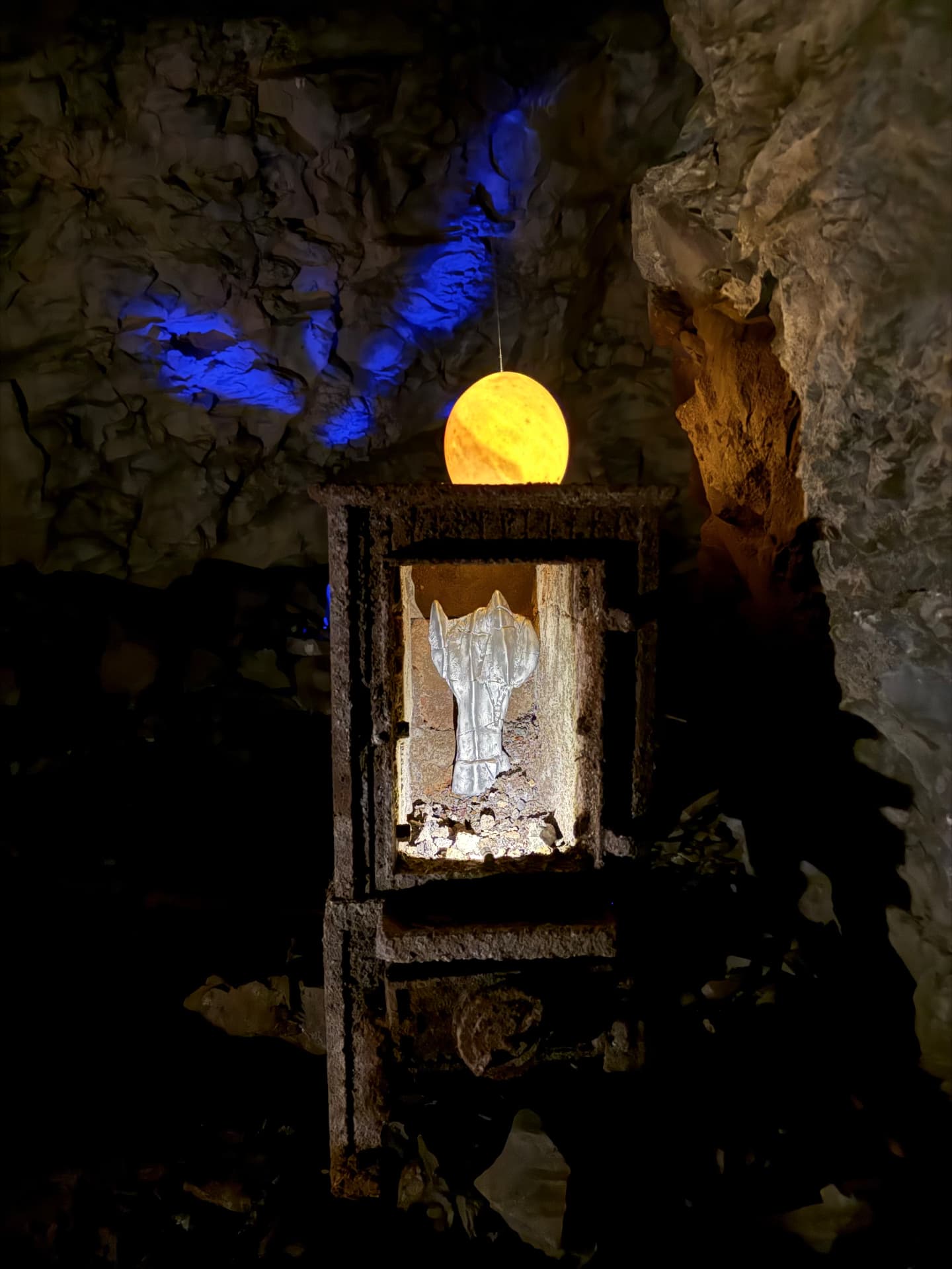 Pale cast form inside the lit cabinet beneath the hanging orb