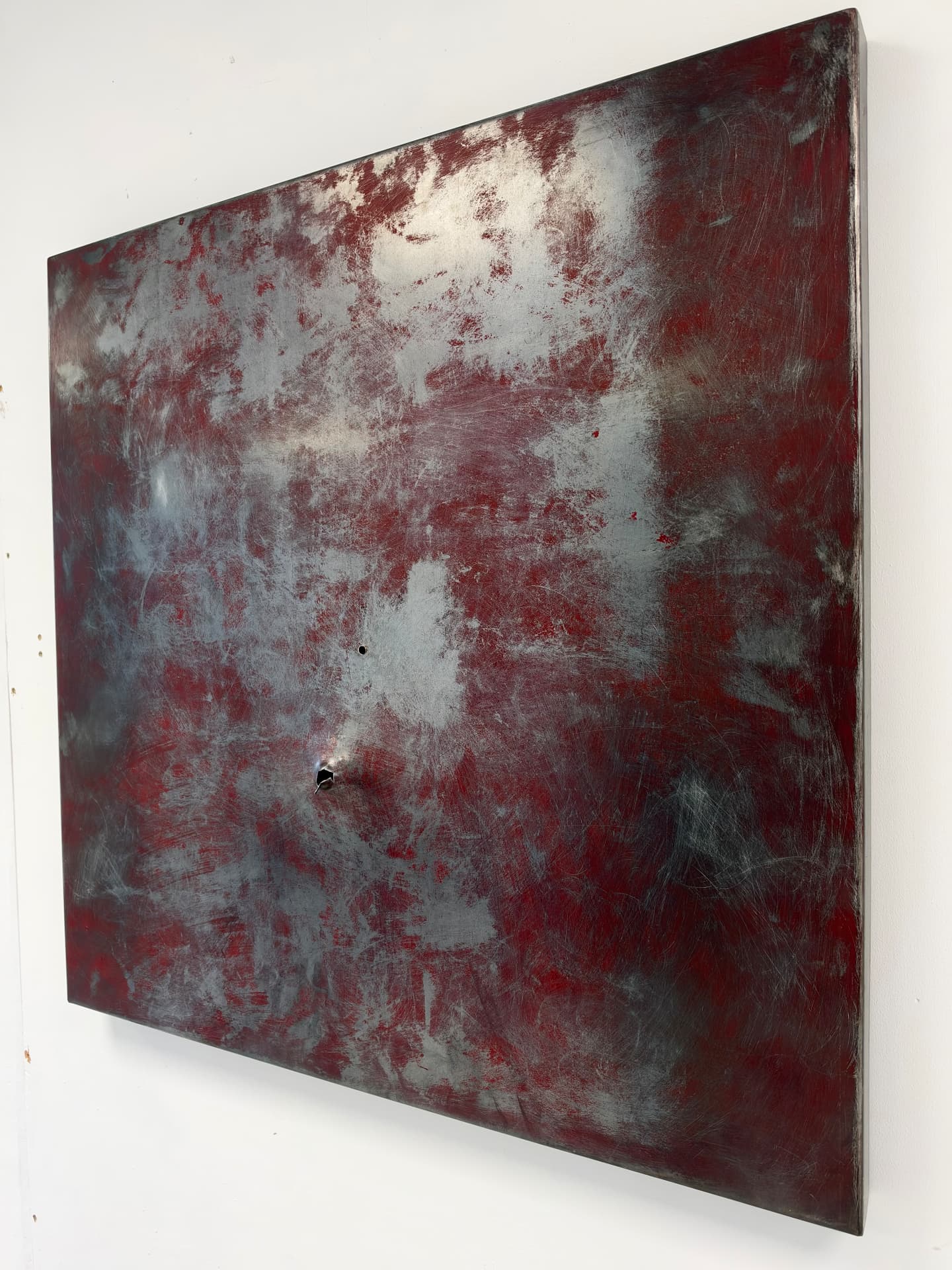 Chris Burden's arm seen from the side, the red and bare steel panel mounted flat against a white wall