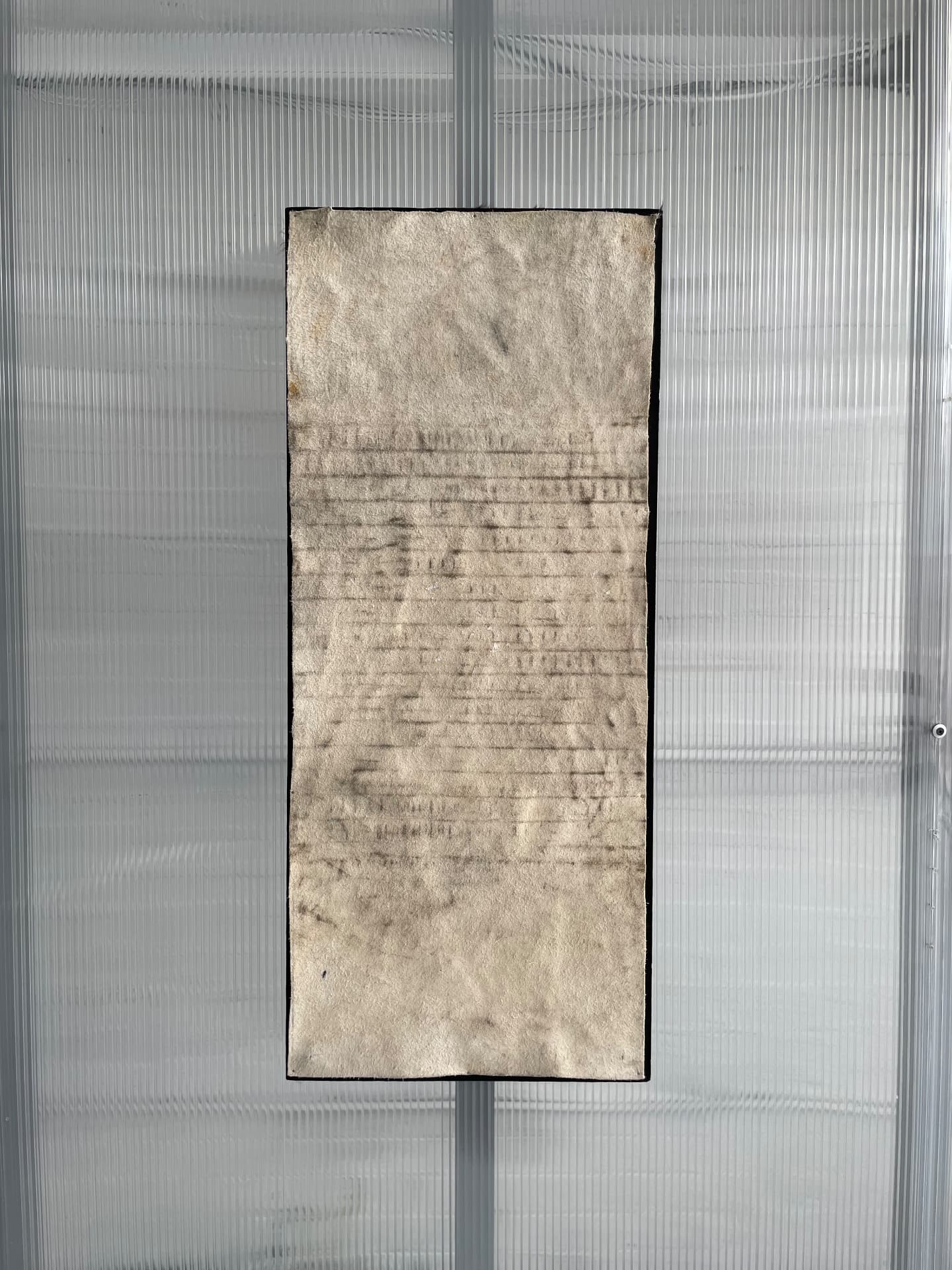 Pale pressed paper panel with faint imprints, mounted on a ribbed plastic wall